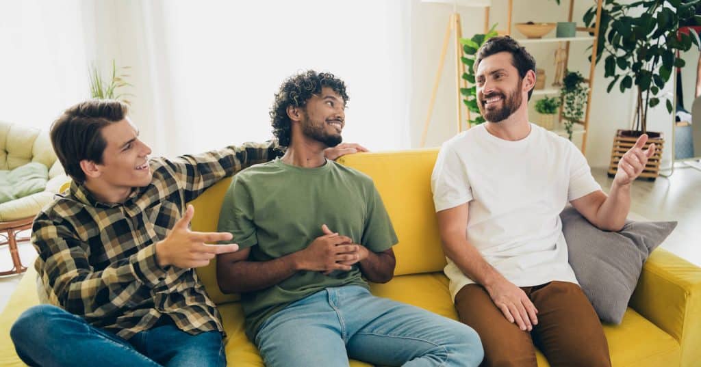 Group of men talking and smiling on a couch, representing community and brotherhood in long-term sobriety programs in San Bernardino.