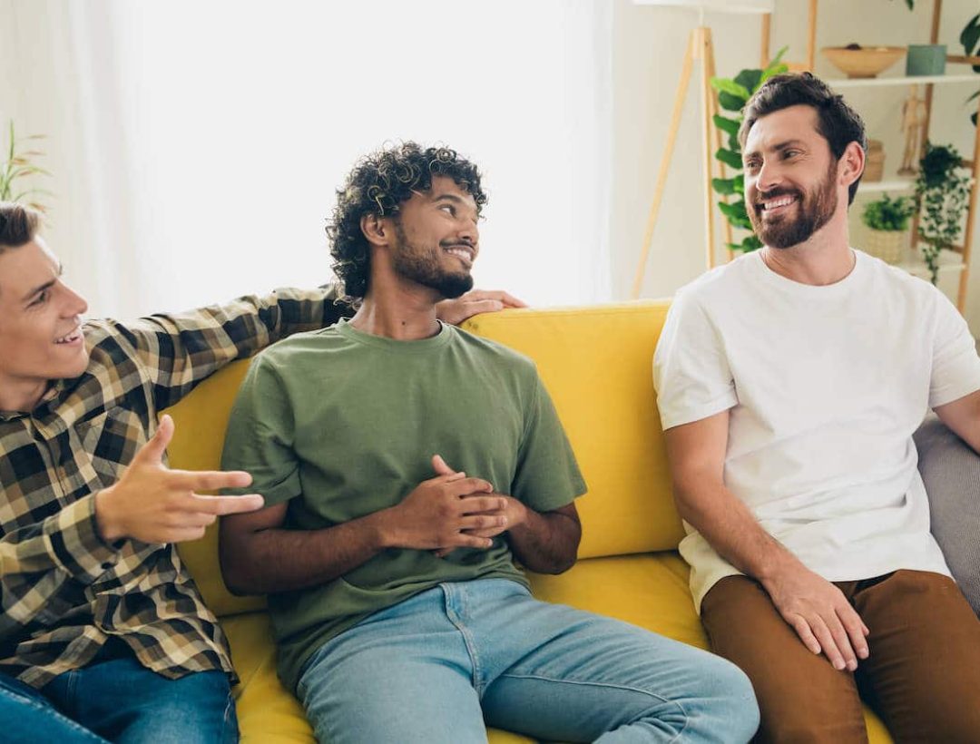 Group of men talking and smiling on a couch, representing community and brotherhood in long-term sobriety programs in San Bernardino.
